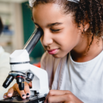 A young woman examines a specimen under a microscope.