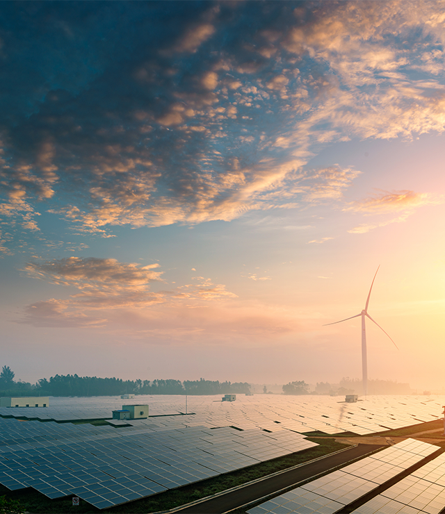 A shot of solar panels and wind turbines, with a sunrise/sunset in the background.