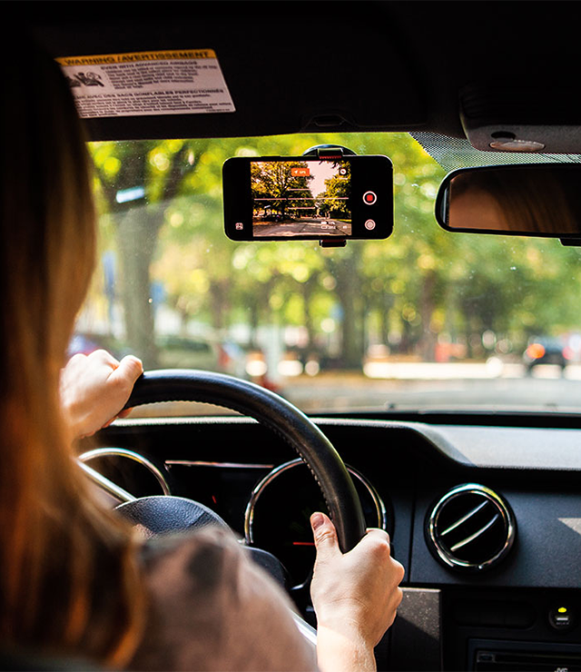 An over-the-shoulder shot of a person driving, using an iPhone as a dashcam.