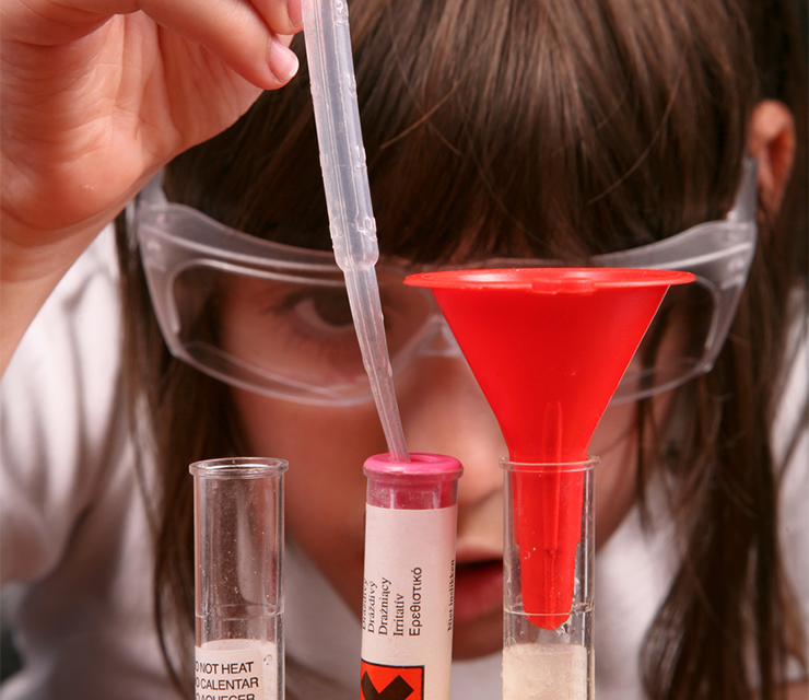 A woman transfers liquid into a test tube inside a science lab.