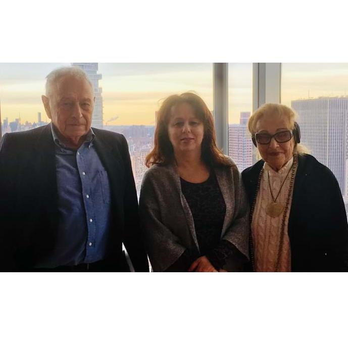 Two parents and their adult daughter all pose together, with the NYC skyline in the background.