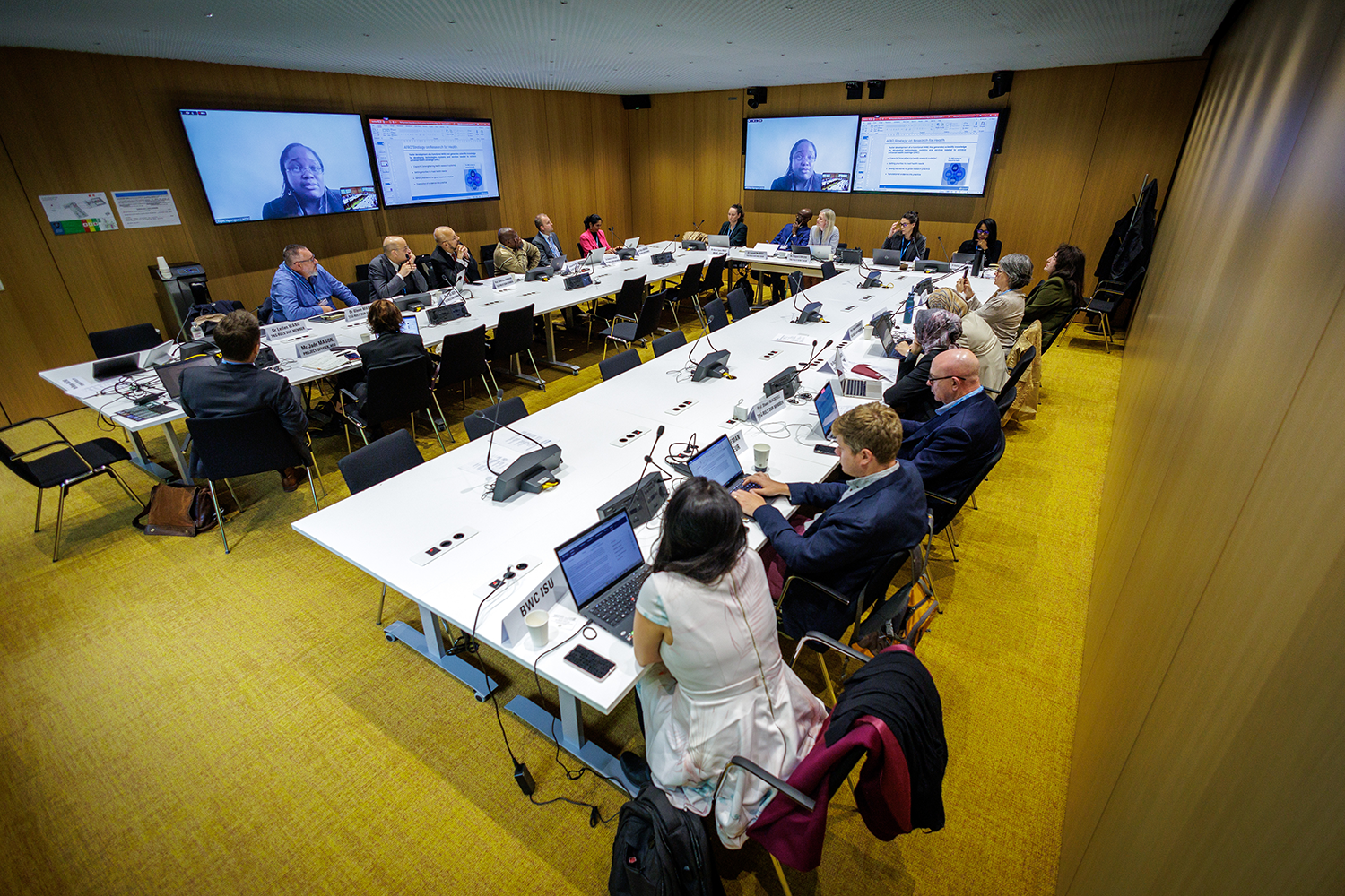A group of people sit around a u-shaped table in a boardroom.