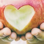 A person holds an apple with a heart shape cut out of it.