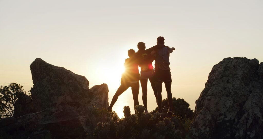 A stock photo of three friends posing together while hiking and watching a sunset/sunrise.