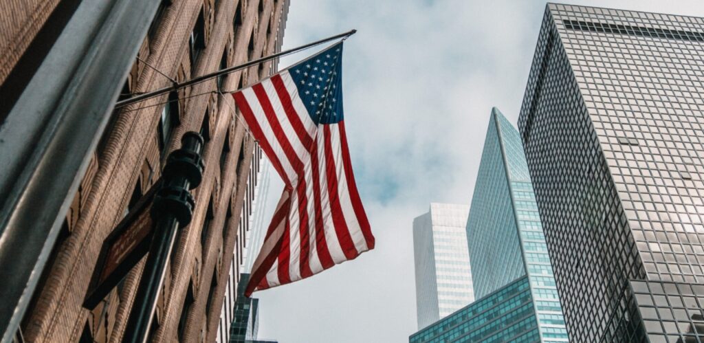 An American flag with tall buildings in the background.